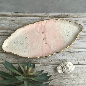 May include: A pink and white ceramic serving tray with a gold rim and a delicate floral design. The tray is oval shaped and has a slightly raised edge.