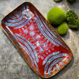 May include: A rectangular ceramic serving tray with a red, blue, and gold design. The tray has a raised rim and a glossy finish.
