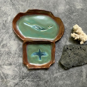 May include: A ceramic serving dish with two sections. The top section features a green glaze with a white narwhal design. The bottom section features a green glaze with a blue bird design.