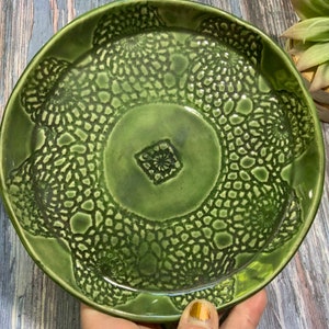 May include: A green ceramic dish with a raised lace pattern. The dish has a square design in the center.