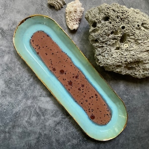 May include: A light blue oval serving dish with a gold rim and a brown speckled center. The dish is on a gray background.
