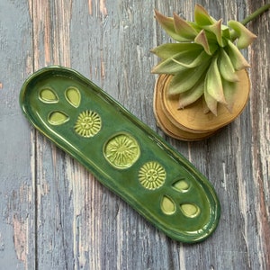 May include: A green ceramic dish with a raised design of flowers and leaves. The dish is oval shaped and has a glossy finish.