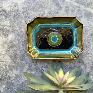 May include: A rectangular ceramic tray with a dark blue center speckled with gold dots. The tray has a teal and green border with gold trim. A circular teal and green design is in the center of the tray.