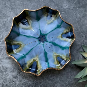 May include: A blue and green ceramic dish with a gold rim and a starburst pattern. The dish has a wavy edge.