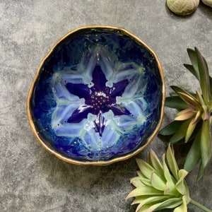 May include: A blue ceramic bowl with a gold rim and a white and purple flower design. The bowl is decorated with gold dots.