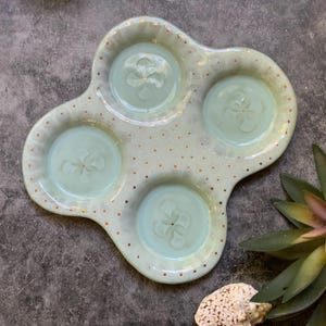 May include: A light blue ceramic serving tray with four indented sections, each with a raised floral design. The tray is decorated with gold dots.