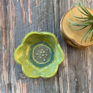 May include: A green and yellow ceramic dish with a flower-like shape and a textured center. The dish has a green and blue rim.