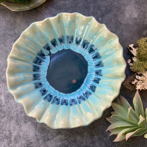 May include: A ceramic bowl with a ruffled edge and a blue and green glaze. The bowl has a deep center with a dark blue glaze.