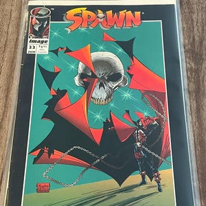 Puede incluir: Portada del cómic Spawn con una calavera, capa roja y cadenas, dentro de una funda protectora. El título "Spawn" está en amarillo y naranja. El número 22 es visible, junto con el logotipo de Image Comics.