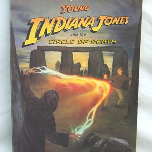 以下が含まれることがあります： 「Young Indiana Jones and the Circle of Death」の表紙には、フードをかぶった人物がエネルギーを呼び出すドラマチックなシーンが描かれています。タイトルは黄色とオレンジ色で、著者の名前が下にあります。