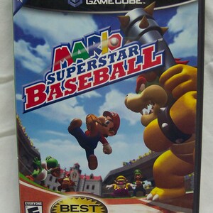May include: Mario Superstar Baseball video game case. The cover features Mario in mid-air, with Bowser and a baseball bat. The game is rated "E" for Everyone and is a "Best Seller". The Nintendo GameCube logo is at the top.