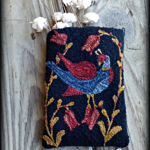 Puede incluir: Una almohada de punto de aguja negra con un pájaro azul y tulipanes rojos en una vid dorada. La almohada está titulada "Tulips In Spring, Vermont Harvest Folk Art by Doreen Frost".