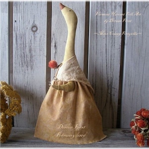 Könnte beinhalten: Eine handgefertigte Folk-Art-Gänse-Puppe mit langem Hals, die ein braunes Kleid und einen weißen Schal trägt und eine getrocknete Blume hält. Die Puppe steht vor einem hölzernen Hintergrund. Der Text "Deron Frost Februar 2007" ist auf dem Kleid der Puppe geschrieben.
