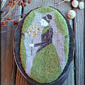 May include: A needlepoint artwork of a woman in a green dress holding a bouquet of flowers. The artwork is framed in a dark wood oval frame. The text "Vermont Harvest Folk Art Original Needlework Creations by Doreen Frost" is below the frame.