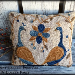 Pode incluir: Uma almofada feita à mão com dois pavões azuis e castanhos com uma grande flor azul no centro. A almofada está sobre um fundo de madeira rústico. "Vermont Harvest Folk Art by Doreen Frost" está escrito abaixo da almofada.
