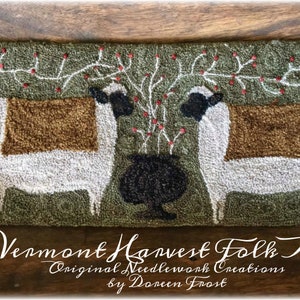 May include: Two white sheep with brown wool on their backs stand on a green background. A black pot with a white rim sits between them. A vine with red berries grows above the pot and sheep. The text "Vermont Harvest Folk Art Original Needlework Creations by Doreen Frost" is at the bottom of the image.