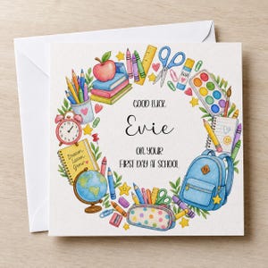 May include: A square greeting card featuring a watercolour illustration of school supplies arranged in a wreath. The text reads: GOOD LUCK Evie ON YOUR FIRST DAY AT SCHOOL. Items include a blue backpack, globe, books, apple, scissors, and crayons.