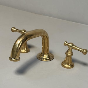 May include: A gold-toned bathroom faucet with two handles and a curved spout. The faucet has a traditional design with a polished finish.