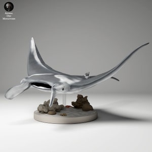 Peut inclure: Une figurine de raie manta de couleur argentée sur un socle blanc avec une scène de récif corallien. La figurine est détaillée avec une surface texturée et une forme réaliste.