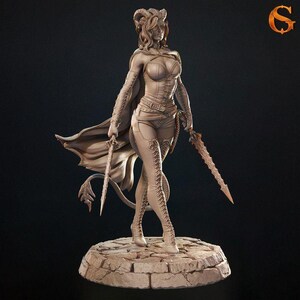 Może przedstawiać: Szczegółowa figurka żeńskiej postaci fantasy, trzymającej dwa miecze. Postać ubrana jest w gorset, szorty i wysokie buty, z peleryną i rogami. Postać stoi na kamiennej podstawie. Ogólny kolor to jasnobrązowy.