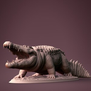 Peut inclure: Modèle imprimé en 3D détaillé d'un crocodile gris, la gueule ouverte, montrant des dents acérées. Le crocodile est en position de marche vers l'avant, la queue levée. Le modèle est sur une base ovale grise.