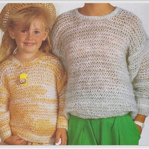 May include: Two people wearing white knit sweaters with a lacy pattern. The sweater on the left is yellow and white, and the sweater on the right is white. The person on the left is wearing a straw hat.
