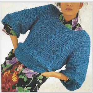 May include: A teal blue knitted jumper with a textured pattern. The jumper has a boat neck and three-quarter sleeves. The sleeves have a textured pattern. The jumper is worn over a floral print top.