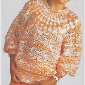 May include: A soft, orange and white striped jumper with a round neckline. The jumper has a geometric pattern at the neckline.