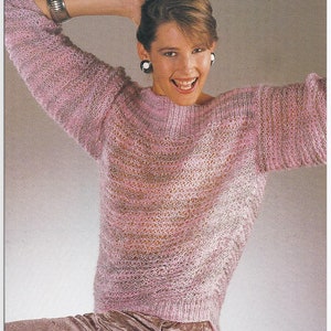 May include: A pink knitted jumper with a loose fit and a slightly open neckline. The jumper has a textured, open-knit design.
