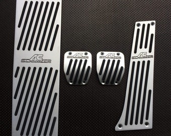 May include: Set of five silver metal car pedal covers with black accents. The covers feature the AC Schnitzer logo and a striped design.