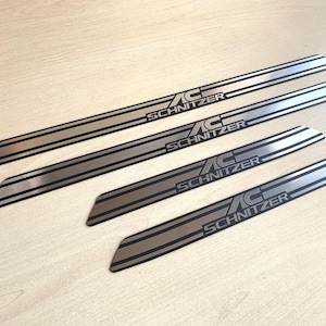 May include: Four silver car door sill trims with the word "Schnitzer" printed in black lettering.