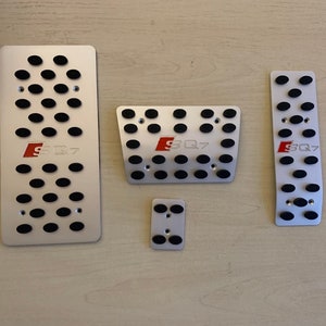 May include: Set of silver-colored car pedal covers with black rubber inserts. Each pedal cover has the red letters "SQ7" printed on it. The set includes four different sized covers.
