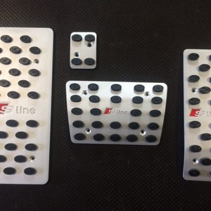 May include: Set of four silver-colored car pedal covers with black rubber studs for grip. Each pedal cover has the red and white "S line" logo. The set includes an accelerator, brake, clutch, and footrest cover.