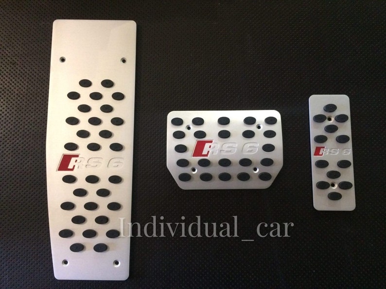 May include: Set of three silver-colored car pedal covers. Each pedal cover has black rubber inserts for grip and the red letters "RS6". The largest pedal cover is rectangular with oval cutouts. The text "Individual_car" is at the bottom.