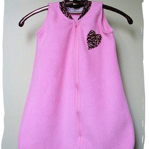May include: Pink fleece sleep sack with a zipper closure and a brown heart-shaped patch with a leopard print design.