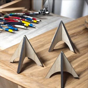May include: Three wooden display stands with a triangular shape and a black painted edge. The stands are made of light wood and have a curved base.