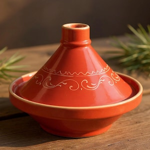 May include: A vibrant red ceramic tagine pot with a conical lid and a wide, shallow base. The lid features a delicate white decorative pattern. The tagine is designed for cooking and serving Moroccan and North African dishes.