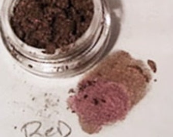 Op de afbeelding: Een klein glazen potje gevuld met een roodbruin poeder met het label "Red Smoke".