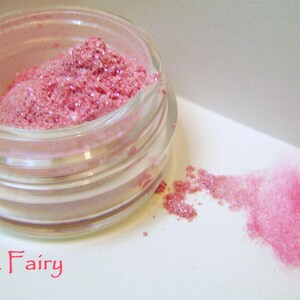 May include: A small glass jar filled with pink glitter makeup. The jar is labeled "Pink Fairy".