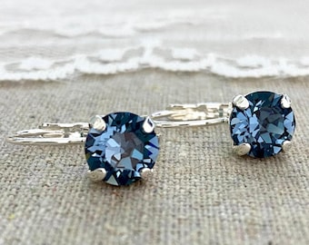 May include: A pair of leverback earrings featuring round, faceted dark blue crystals set in silver-toned metal prongs. The earrings have a classic design with a secure hinged closure mechanism, showcasing the deep blue color and reflective surfaces.