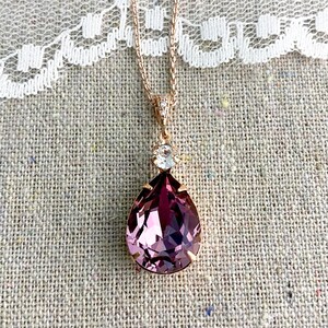 Puede incluir: Un collar de oro rosa con un colgante grande en forma de l&aacute;grima. El colgante es de color p&uacute;rpura oscuro con una superficie facetada. Un peque&ntilde;o cristal transparente se encuentra encima del colgante. El collar se muestra sobre un fondo de lino neutro.