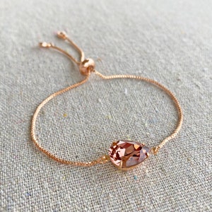 K&ouml;nnte beinhalten: Verstellbares Armband in Ros&eacute;gold mit einem tropfenf&ouml;rmigen, hellbraunen Kristall. Das Armband hat eine feine Kette und einen Schiebeverschluss f&uuml;r eine individuelle Passform. Der Kristall ist das Hauptmerkmal des Armbands.