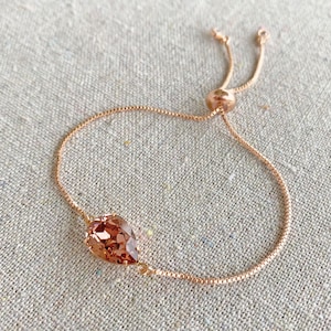K&ouml;nnte beinhalten: Verstellbares Armband aus Ros&eacute;gold mit einem tropfenf&ouml;rmigen, pfirsichfarbenen Kristall. Die filigrane Kette hat ein Box-Link-Design, und das Armband wird mit einer Gleitperle verstellt. Ein schlichtes und elegantes Schmuckst&uuml;ck.