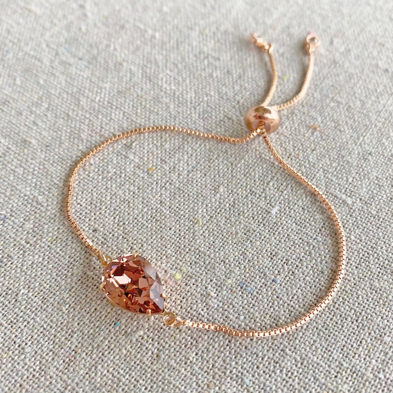 K&ouml;nnte beinhalten: Verstellbares Armband aus Ros&eacute;gold mit einem tropfenf&ouml;rmigen, pfirsichfarbenen Kristall. Die filigrane Kette hat ein Box-Link-Design, und das Armband wird mit einer Gleitperle verstellt. Ein schlichtes und elegantes Schmuckst&uuml;ck.