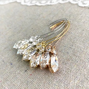 May include: An assortment of crystal hair pins in silver, gold, and rose gold tones. Each pin features a marquise-cut crystal pendant and smaller accent crystals. The pins are arranged on a neutral fabric background.