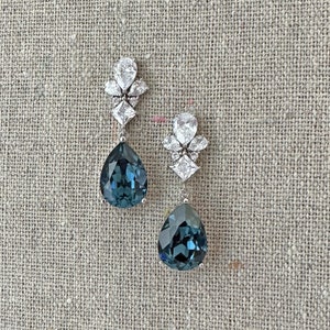 Puede incluir: Un par de pendientes colgantes con grandes cristales azul oscuro facetados en forma de pera, suspendidos de un engaste plateado. La parte superior de cada pendiente está adornada con un grupo de cristales claros más pequeños en formas de pera y cuadrado.