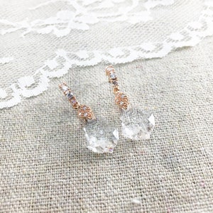 May include: Rose gold drop earrings with clear, faceted crystal pendants. The earrings have a delicate design with small, sparkling crystals along the top. The crystals are set in a geometric pattern, adding elegance to the jewellery.