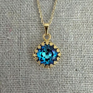 May include: A gold-colored necklace with a pendant featuring a large, faceted, teal-blue gemstone. The gemstone is set in a decorative gold-colored bezel. The necklace chain is also gold-colored.