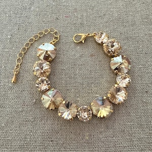 Puede incluir: Un brazalete dorado con múltiples cristales redondos de color champán. El brazalete tiene una delicada cadena para ajustar el tamaño y un cierre seguro. Los cristales están facetados, captando la luz y creando un efecto brillante.