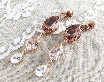 May include: Elegant rose gold earrings with a cascading design. Each earring features a large, teardrop-shaped brown crystal, followed by smaller pink and clear crystals. The earrings are set against a neutral background.